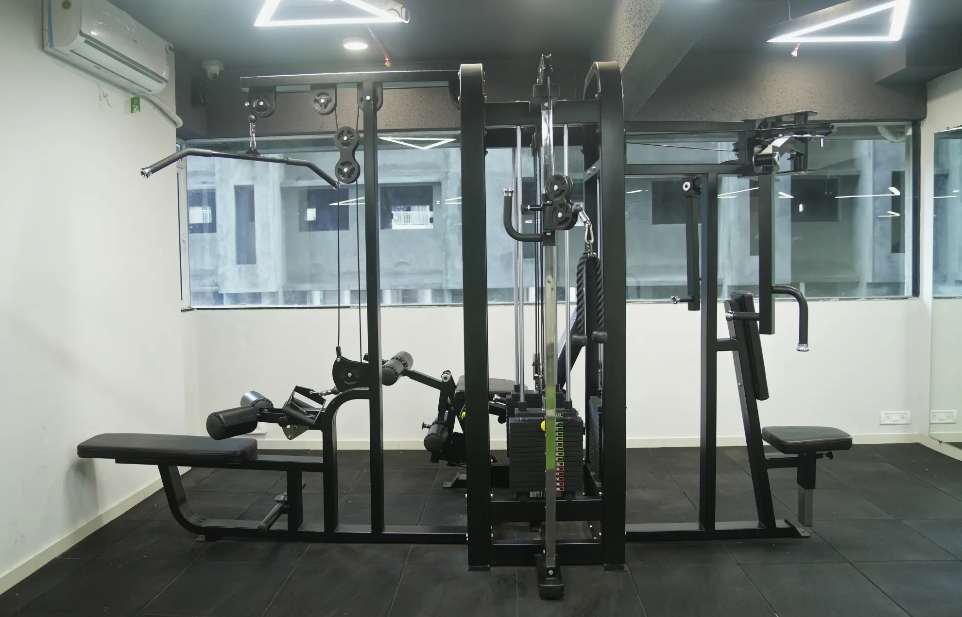 Multi-gym workout station with cable machine and benches in a modern indoor fitness center.